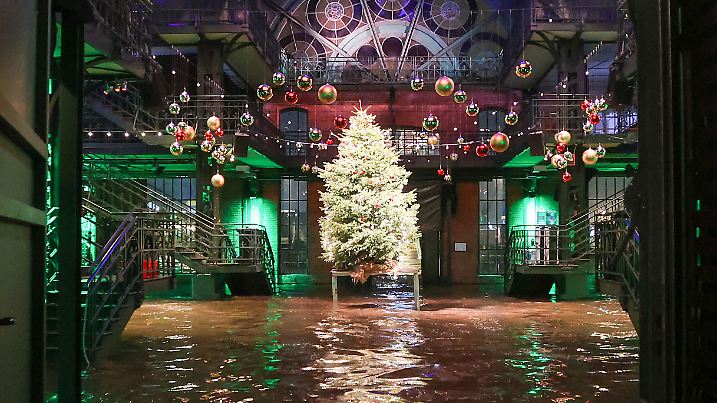 dpatopbilder - 20.12.2024, Hamburg: Das Wasser der Elbe wird bei einer Sturmflut auf den Hamburger Fischmarkt gedrückt und steht in der Fischauktionshalle. Dort ist Weihnachtsschmuck und ein Weihnachtsbaum auf einem Podest zu sehen. Foto: Bodo Marks/dpa +++ dpa-Bildfunk +++