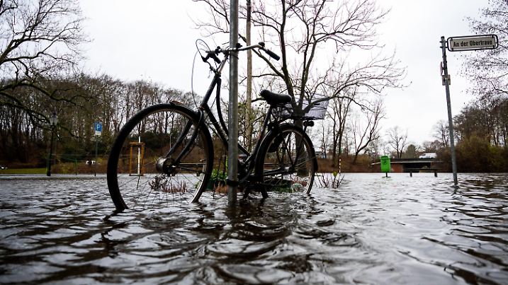 09.12.2024, Schleswig-Holstein, Lübeck: Ein Fahrrad steht in der Altstadt im Wasser der Trave, die über die Ufer tritt. Stürmisches Wetter sorgt für hohe Wasserstände. Foto: Daniel Bockwoldt/dpa +++ dpa-Bildfunk +++