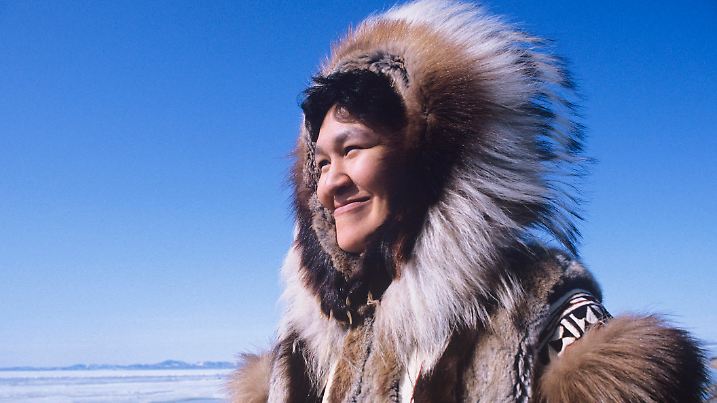 Smiling Eskimo woman wearing traditional clothing in wind against clear blue sky