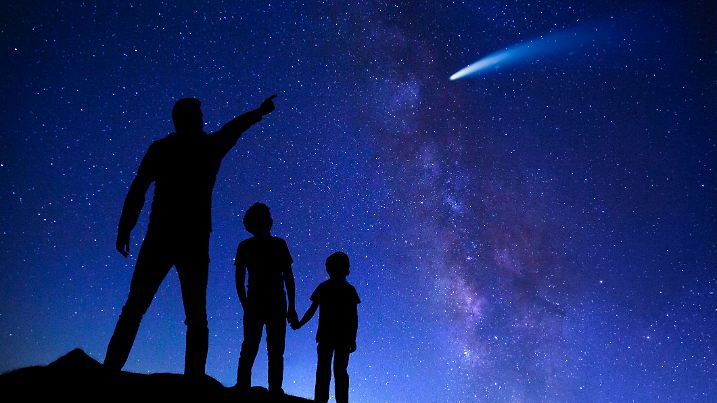 Silhouette of father with two boys on the night of Milky Way, looking at the sky surprised by unexpected comet.