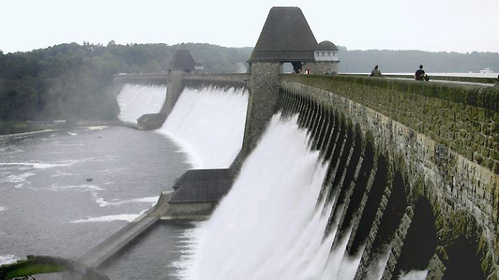 Besucher gehen über die Möhnetalsperre am Freitag (10.08.2007). Nach tagelangem Dauerregen ist die Möhnetalsperre im Sauerland, südlich von Arnsberg, erstmals seit mehr als 20 Jahren wieder übergelaufen. Bis zu 40 Kubikmeter Wasser pro Sekunde strömten dabei durch die Hochwasserüberläufe unter der Mauerkrone und stürzten tosend rund 35 Meter in die Tiefe. Dabei entstand wie bei einem hohen Wasserfall  eine Gischt, die da Bruchsteinmauerwerk in einen weißen Wasserschleier hüllte. Foto: Andreas Dunker dpa/lnw +++(c) dpa - Bildfunk+++