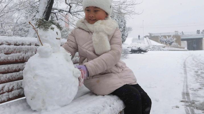27.01.2025, Nordkorea, Pothonggang: Ein Mädchen sitzt auf einer Bank und spielt mit einem Schneemann im Bezirk Pothonggang im Schnee. Foto: Cha Song Ho/AP/dpa +++ dpa-Bildfunk +++