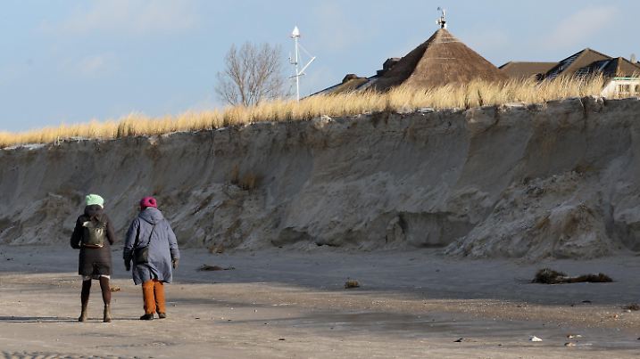 13.01.2025, Mecklenburg-Vorpommern, Wustrow: Spaziergänger gehen auf der Ostseehalbinsel Fischland an der meterhohen Abbruchkante der beschädigten Düne entlang. Die Sturmflut vom vergangenen Wochenende hat in einigen Ostseebädern deutliche Schäden hinterlassen. Foto: Bernd Wüstneck/dpa +++ dpa-Bildfunk +++