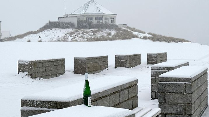 12.02.2025, Niedersachsen, Norderney: Eine Flasche steht auf einer mit Schnee bedeckten Bank vor dem Café Marienhöhe an der Hohen Düne auf der ostfriesischen Insel Norderney. Der Deutsche Wetterdienst erwartet heute für Ostfriesland und das Emsland leichten Schneefall - auch in den kommenden Tagen soll es in Niedersachsen mancherorts schneien. Foto: Volker Bartels/dpa +++ dpa-Bildfunk +++