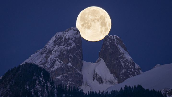 ARCHIV - 06.02.2023, Schweiz, Aigle: Der Vollmond geht im Februar 2023 in der Schweiz von Aigle aus gesehen hinter den Bergen unter, darunter die Zwillingsgipfel von Les Jumelles im Chablais Valaisan. (zu dpa: «Wenn sich der Blick nach oben lohnt - Schneemond im Februar») Foto: Anthony Anex/KEYSTONE/dpa +++ dpa-Bildfunk +++