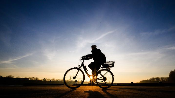 03.02.2025, Niedersachsen, Hannover: Die Silhouette einer Frau auf einem Fahrrad zeichnet sich vor aufgehenden Sonne ab. Foto: Julian Stratenschulte/dpa +++ dpa-Bildfunk +++