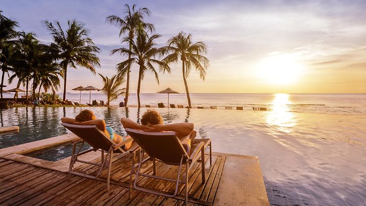beach holidays for couple in luxury hotel, banner background with copyspace, man and woman relaxing near swimming pool at sunset