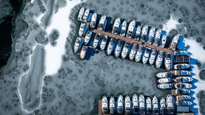 19.02.2025, Mecklenburg-Vorpommern, Waren (Müritz): Haus- und Charterboote liegen im Hafen am Fischerhof Eldenburg in der Mecklenburgischen Seenplatte im Eis. (Luftaufnahme mit einer Drohne). Das Frostwetter der vergangenen Tage sorgt auf den Seen und Kanäle für eine teilweise geschlossenen Eisdecke. Foto: Jens Büttner/dpa +++ dpa-Bildfunk +++