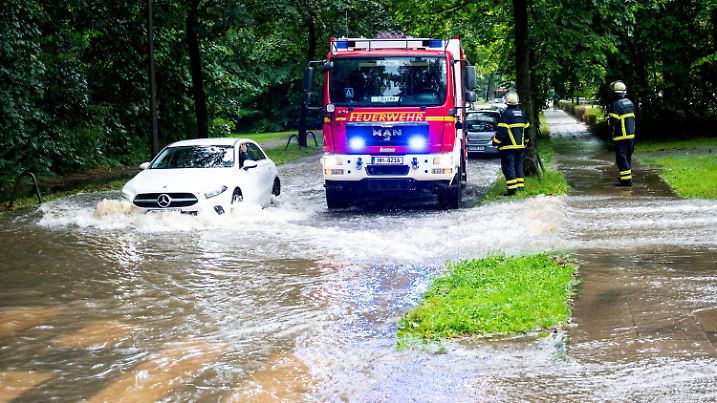 ARCHIV - 07.08.2024, Hamburg: Ein Auto fährt im Stadtteil Lohbrügge durch eine überschwemmte Straße, auf der ein Feuerwehrfahrzeug steht. (zu dpa: «Hamburg will sich besser auf den Klimawandel vorbereiten») Foto: Daniel Bockwoldt/dpa +++ dpa-Bildfunk +++