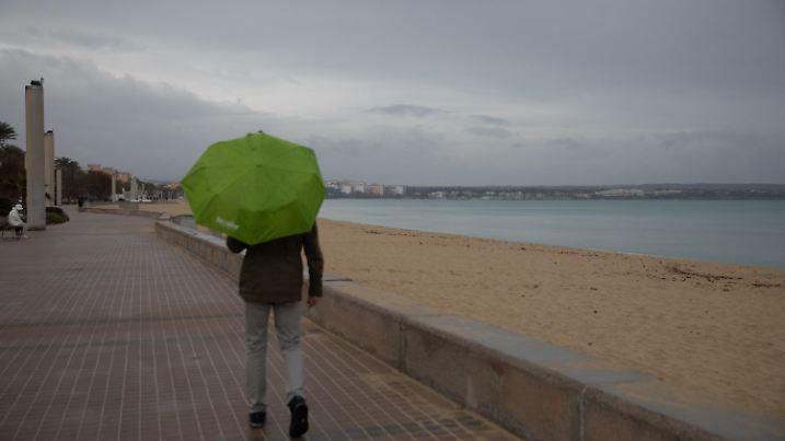 06.03.2025, Spanien, Palma: Ein Mann geht an einem regnerischen Tag mit einem Regenschirm am Arenal-Strand auf Mallorca spazieren. In den nächsten Tagen wird es auf Mallorca instabiles Wetter mit einem kalten Sturm geben. Foto: Clara Margais/dpa +++ dpa-Bildfunk +++