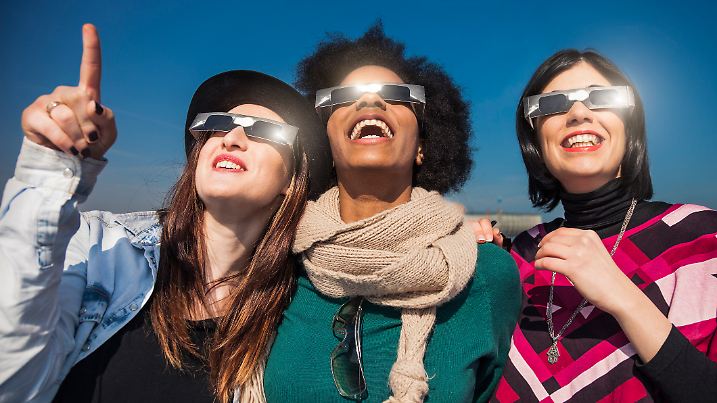 Group of female friends have fun together during a solar eclipse event. Their looking and pointing to the sun wearing the typical glasses normally used to watch a solar eclipse.