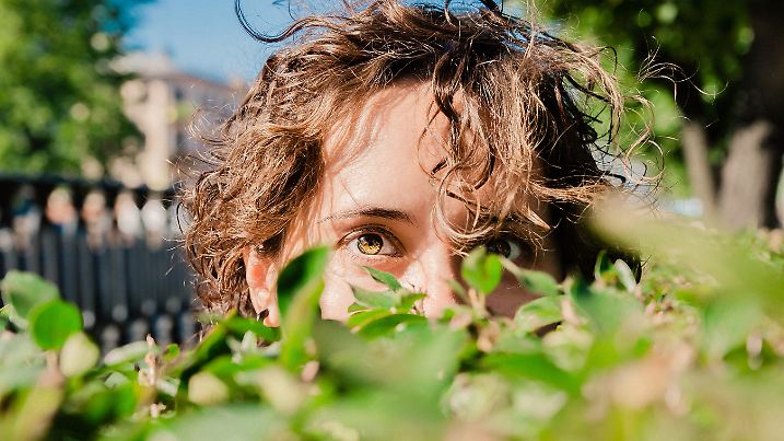 Frau schaut hinter Blättern vor. Die Temperaturen liegen bei weniger als 15 Grad.