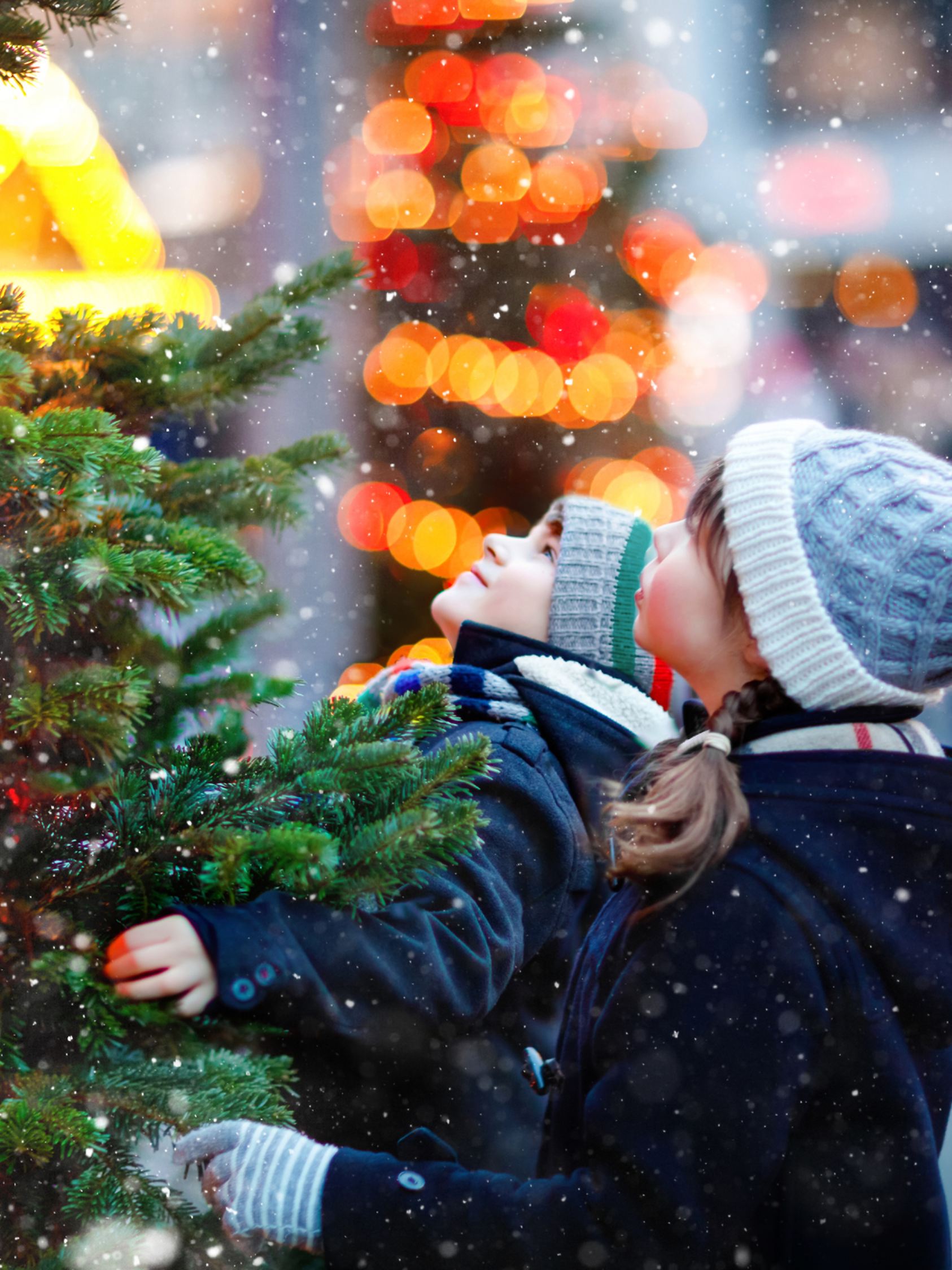 Two little kids, boy and girl having fun on traditional Christmas market during strong snowfall. Happy children enjoying traditional family market in Germany. Twins standing by illuminated xmas tree