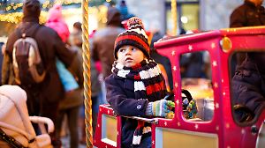 Funny little kid boy on a carousel at Christmas funfair or market, outdoors. Happy child having fun. Traditional xmas market in Germany, Europe. Holiday, children, lifestyle concept.