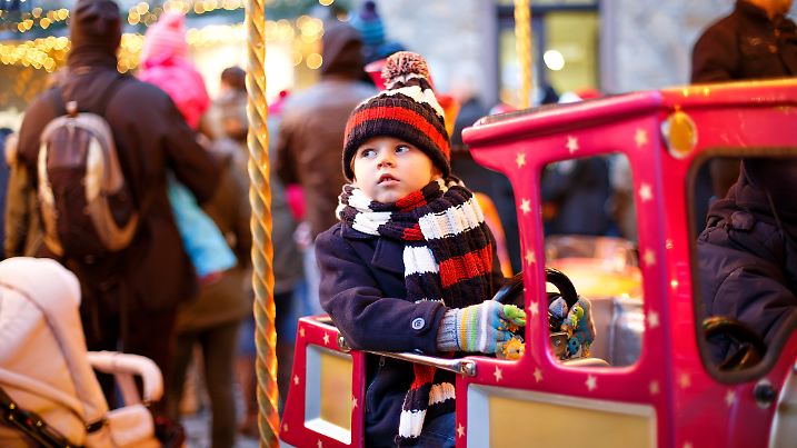 Funny little kid boy on a carousel at Christmas funfair or market, outdoors. Happy child having fun. Traditional xmas market in Germany, Europe. Holiday, children, lifestyle concept.