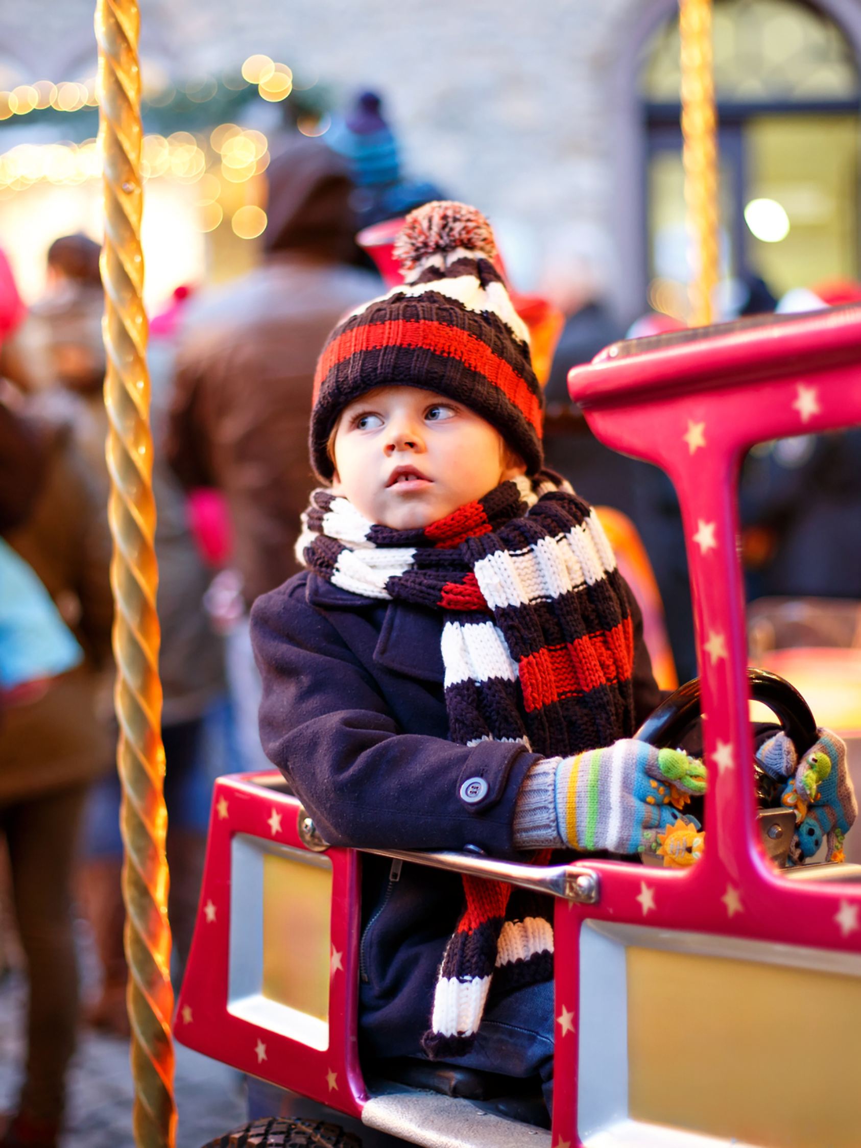 Funny little kid boy on a carousel at Christmas funfair or market, outdoors. Happy child having fun. Traditional xmas market in Germany, Europe. Holiday, children, lifestyle concept.