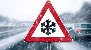 16 December: Sign warning of snow, cold and icy conditions in a snowstorm on the highway with moving vehicles PHOTOMONTA