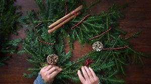 Immergrüne Zweige werden mit Dekorationen für einen Adventskranz arrangiert.