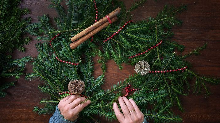 Immergrüne Zweige werden mit Dekorationen für einen Adventskranz arrangiert.
