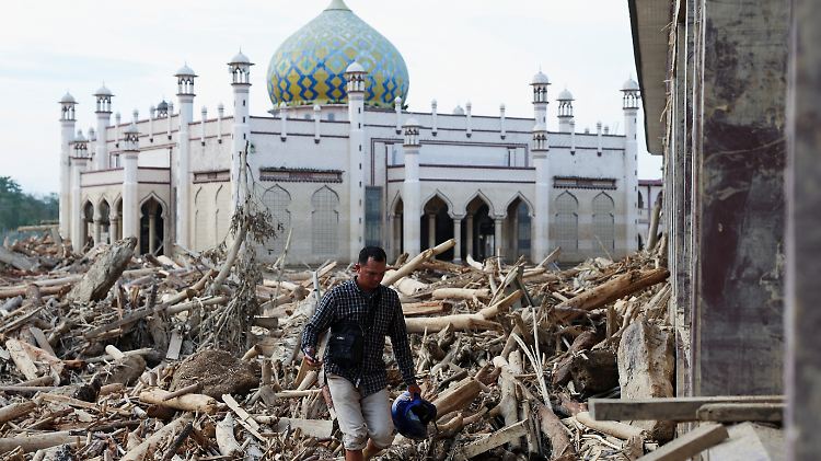 A survivor walks through tree trunks stranded at a mosque in an area affected by a deadly flash flood following heavy rains in Karang Baru