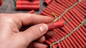 Bavaria, Germany - December 17, 2025: A hand holds a single firecracker in front of several fireworks. The close-up serv