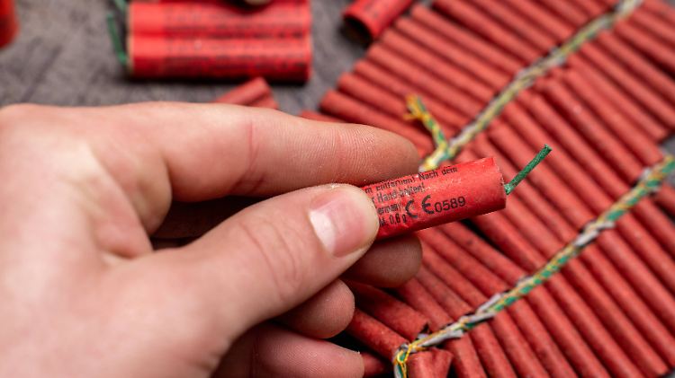 Bavaria, Germany - December 17, 2025: A hand holds a single firecracker in front of several fireworks. The close-up serv