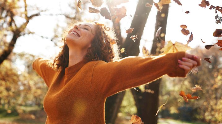 Redhead woman with arms outstretched enjoying autumn leaves falling at park model released, Symbolfoto, ABIF02074