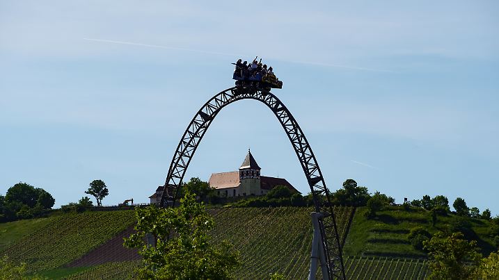 Spaß auf dem höchsten Punkt der Achterbahn „Karacho“ im Erlebnispark „Tripsdrill“ – im Hintergrund Weinberge und eine Kirche.