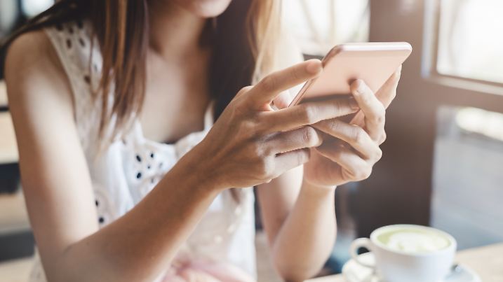 Junge Frau mit Smartphone und Kaffeetrinken im Café