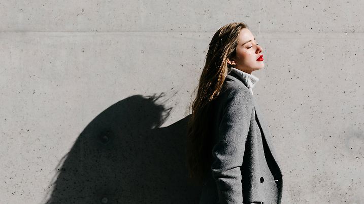 Eine junge Frau in einem grauen Mantel genießt die Sonne.