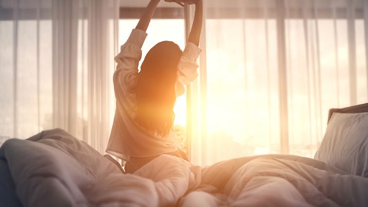 Happy woman stretching in bed after waking up. 