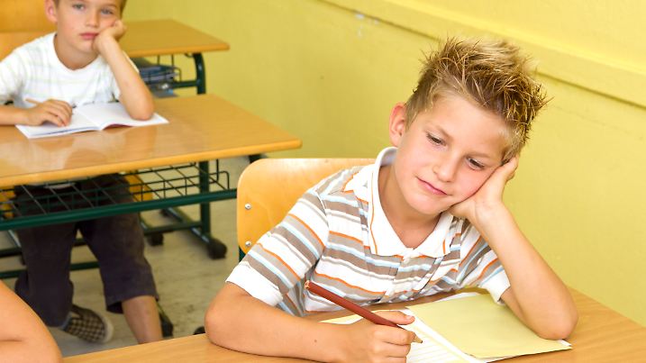 Photo shows two little schoolboys. Both are feeling boring during lesson in school. 