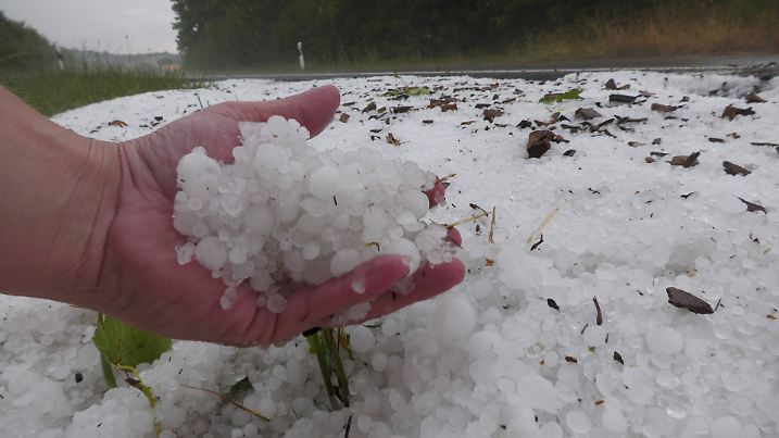Hagel im Hochsommer: Eine Hand voll Eis – dahinter eine schneeweiße Landschaft wie im Winter.