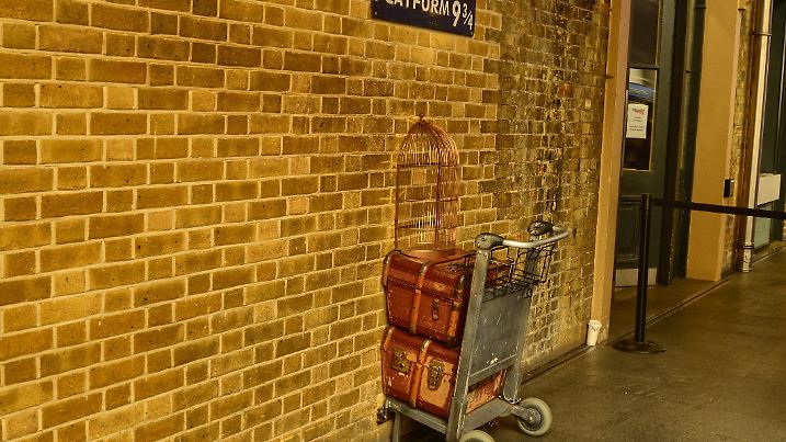 London, United Kingdom, June 2018. Platform 9 and 3/4 at Kings Cross Station, London. A trolly stuck in the wall where fans emulate the Harry Potter adventures. A service assistant for the photo.