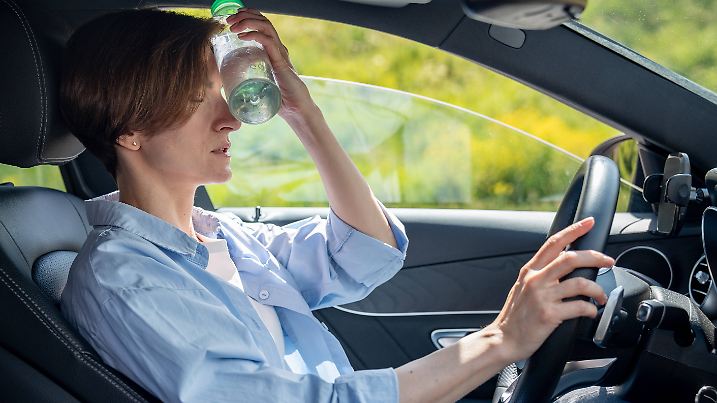 Heißes Wetter für Autofahrer. Müde von der Hitze Frau im Auto nehmen Pause Kühlung Stirn mit kalten Flasche