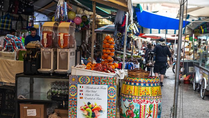 Palermo, Italy - May 13, 2023: Orange juice in a fruit shop in Ballaro Market, street food market with people around in Palermo, Sicily, Italy