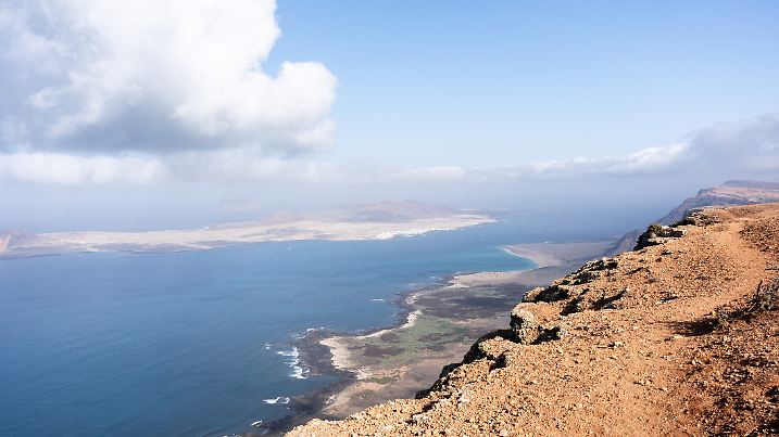 Panoramic view of La Graciosa island, revealing volcanic landscape, azure waters, and dramatic cloud-filled sky from Mirador del Rio viewpoint
