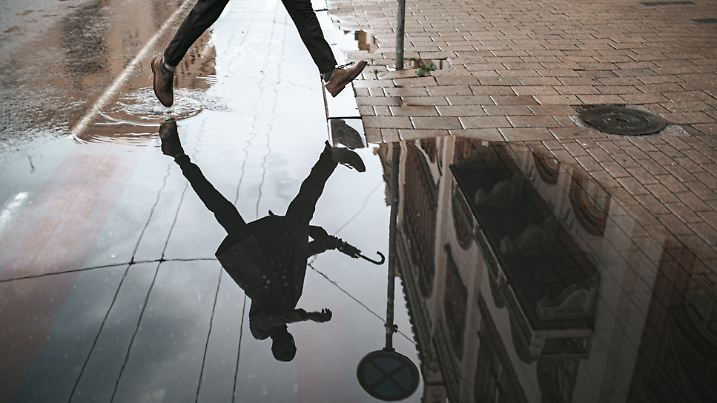 Low section of a man walking down the wet street with reflection in the water