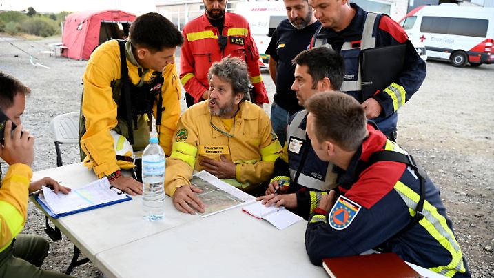Deutsche und spanische Feuerwehrmänner sitzen zur Einsatzbesprechung zusammen. Speziell ausgebildete Einsatzkräfte der Feuerwehr sind aus Deutschland angereist, um bei der Bekämpfung von Waldbränden zu helfen.