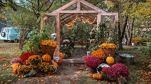 Ein rustikales Gewächshaus zeigt leuchtende Herbstblumen und Kürbisse, umgeben von farbenfrohem Laub. Die Szenerie strahlt eine warme Atmosphäre aus – perfekt für herbstliche Treffen und Feste.
