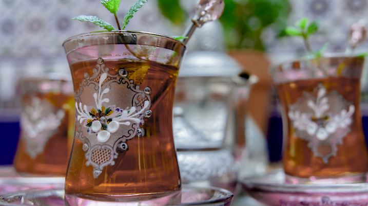 Maurischer Tee mit Minze, traditionelles marokkanisches Getränk in verzierten Kristallgläsern, silberne Teekanne und Zuckerdose im Hintergrund