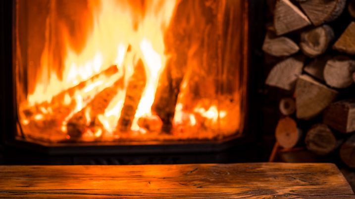 Old wooden table and fireplace with warm fire at the background.