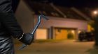 Einbrecher in der Dunkelheit mit Brechstange vor einem Haus 