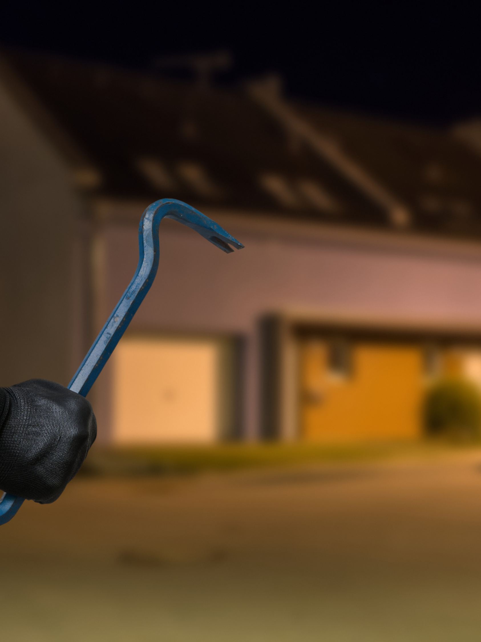 Einbrecher in der Dunkelheit mit Brechstange vor einem Haus 