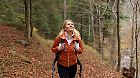 
A happy woman enjoys a refreshing hike in an autumn forest, wearing a puffy orange jacket and carrying a backpack. The autumn foliage provides a picturesque and serene natural backdrop.