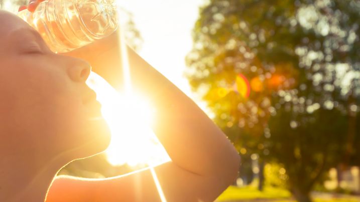 Woman using water bottle to cool down. Fitness and wellbeing concept with female athlete cooling down on a city street. She is holding a water bottle to her head to cool down. The sun is low creating long shadows and some lens flare. Copy space