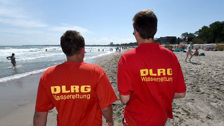 DLRG-Helfer gehen am 22.07.2014 über den Ostseestrand von Timmendorfer Strand (Schleswig-Holstein). Wegen starker Strömung herrscht hier ein Badeverbot. Nach den tödlichen Badeunfällen an der Ostsee hat die Polizei an die Badegäste appelliert, rote Flaggen der DLRG und direkt am Wasser aufgestellte Hinweisschilder zu beachten. Foto: Carsten Rehder/dpa (Zu dpa"Polizei mahnt Badegäste nach Unfällen zur Besonnenheit" vom 22.07.2014) +++(c) dpa - Bildfunk+++