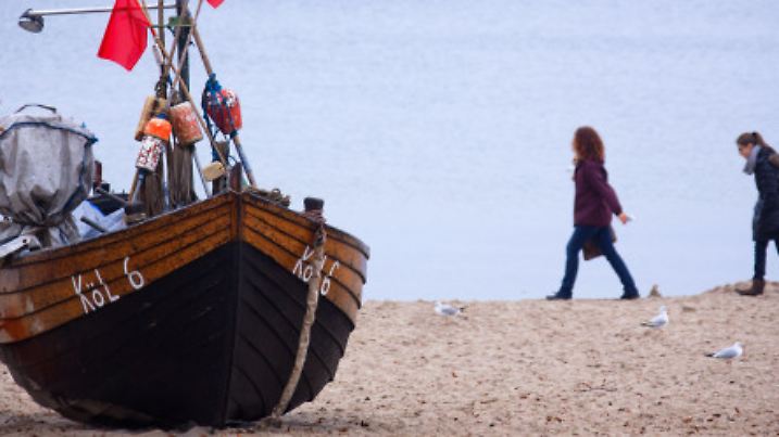 Spaziergänger sind am 03.11.2013 am Strand von Kölpinsee (Mecklenburg-Vorpommern) auf der Ostseeinsel Usedom unterwegs und gehen an einem auf dem Strand liegenden Fischerboot mit den Markierungsfähnchen für Stellnetze vorbei. Foto: Jens Büttner/dpa +++(c) dpa - Bildfunk+++
