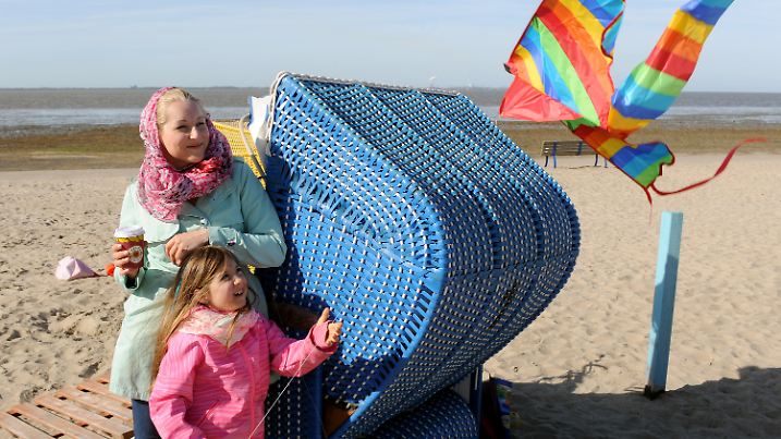 Katrin Topalli aus Bielefeld genießt am 20.04.2015 zusammen mit ihrer Tochter Adelina, die einen Drachen steigen lässt, den Sonnenschein am Strand von Dangast (Niedersachsen). Bei Temperaturen um die 15 Grad Celsius ist es an der niedersächsische Nordseeküste zwar nicht allzu warm, aber sonnig. Foto: Ingo Wagner/dpa +++(c) dpa - Bildfunk+++