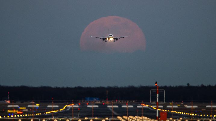 19.02.2019, Hessen, Frankfurt/Main: Ein Passagierflugzeug befindet sich am Frankfurter Flughafen im Landeanflug, während im Hintergrund der Vollmond aufgeht. Foto: Silas Stein/dpa +++ dpa-Bildfunk +++